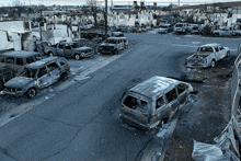 a row of burned out cars are parked on the side of a road