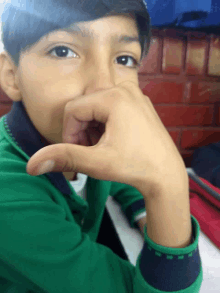 a young boy in a green shirt covering his mouth with his hand