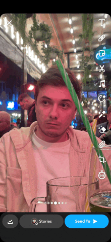 a man sitting at a table with a glass of beer and a green straw in front of his face