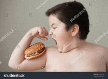 a shirtless boy is holding a hamburger in his hand .