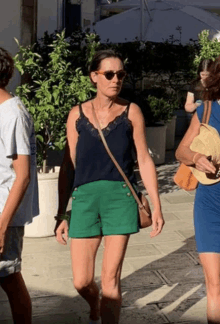 a woman wearing green shorts and a black tank top is walking down the street