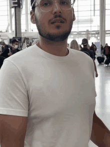 a man wearing glasses and a white t-shirt is standing in an airport