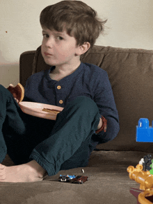 a young boy is sitting on a couch eating a donut