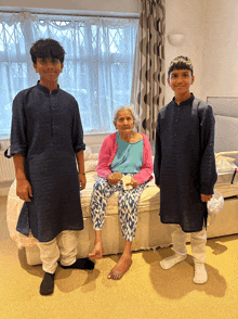 an elderly woman sits on a bed with two young boys standing around her