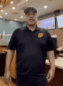 a man wearing a black shirt with a yellow logo on it is standing in front of a counter in a restaurant .