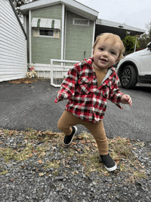 a little boy wearing a plaid shirt is standing in front of a green house