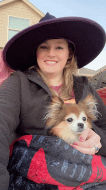 a woman in a witch hat holds a small dog in her arms