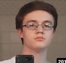 a young man wearing glasses is taking a selfie with his phone in front of a mirror .