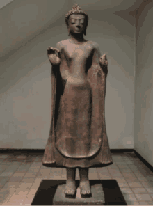 a statue of a buddha is standing in a room with a staircase in the background