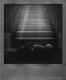 a black and white photo of a woman laying on the floor under stairs