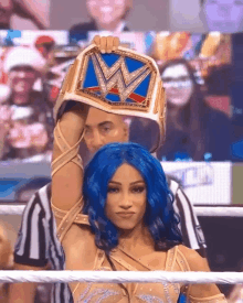 a woman with blue hair is holding up a wrestling championship belt with the letter w on it