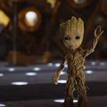 a small figurine of groot from guardians of the galaxy is standing on a table with his arms outstretched .