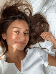 a woman in a white shirt is laying on a bed and smiling