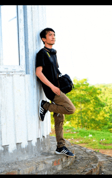 a young man leaning against a wall with headphones on his neck