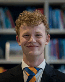 a young man with curly hair wearing a suit and tie is smiling .