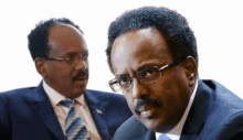 a man with glasses and a mustache is sitting next to another man in a suit