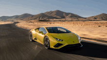 a yellow sports car is driving down a desert road with mountains in the background