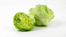 two heads of lettuce on a white surface one of which is cut in half