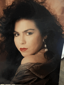 a woman wearing a leather jacket and pearl earrings looks at the camera