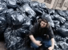 a man is squatting down in front of a pile of black garbage bags .