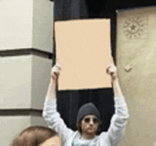 a man in a hat and sunglasses is holding a sign over his head .