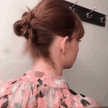 a woman in a pink floral shirt has her hair in a bun