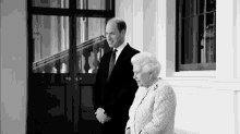 a black and white photo of a man and a woman standing next to each other in front of a door .