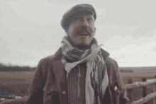 a man wearing a scarf and a hat stands in front of a field