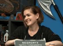 a woman sitting behind a sign that says negaoryx twitch.tv/negaoryx