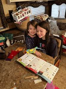 two little girls are sitting at a table reading a book that says " tiny " on it