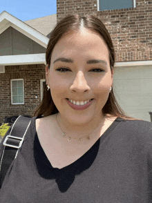 a woman wearing a necklace with the letter h on it smiles in front of a house