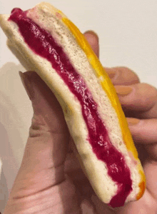 a close up of a person holding a sandwich with a purple jelly filling