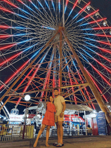 a man and woman are posing in front of a ferris wheel with ice cream in the background