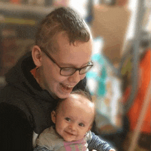 a young boy wearing glasses is holding a baby in his arms and smiling .