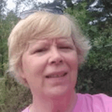 a close up of a woman 's face in a pink shirt with trees in the background .