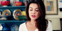 a woman in a white sweater is standing in front of a shelf with bowls and plates on it .