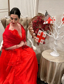 a woman in a red dress sits in a chair in front of a table with flags on it