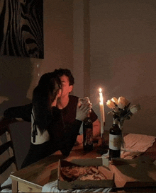 a man and a woman kissing at a table with a box of pizza and a bottle of wine