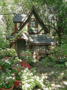 a small house is surrounded by flowers and trees in the middle of a forest .