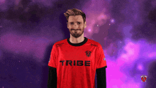 a man wearing a red tribe shirt stands in front of a purple background