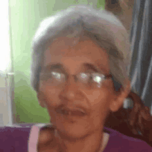 an older woman wearing glasses and a purple shirt is smiling for the camera .