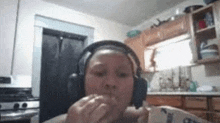 a woman wearing headphones is sitting in a kitchen eating a sandwich .