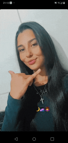 a woman with long black hair and a cross necklace is giving a thumbs up