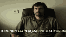 a man with a beard is sitting in a chair with the words " toronun yayin acmasini bekliyorum " written below him