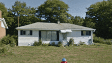 a white house with black shutters sits in the middle of a lush green field