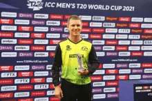 a man in an austria jersey holds a trophy in front of a backdrop for the t20 world cup 2021