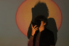 a man with curly hair is standing in front of a projection of the sun