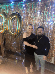 a man and a woman pose for a picture in front of a 30 balloon