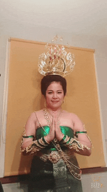 a woman with a crown on her head is wearing a green dress and gold gloves