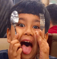 a young boy holds a spoon and a fork to his face